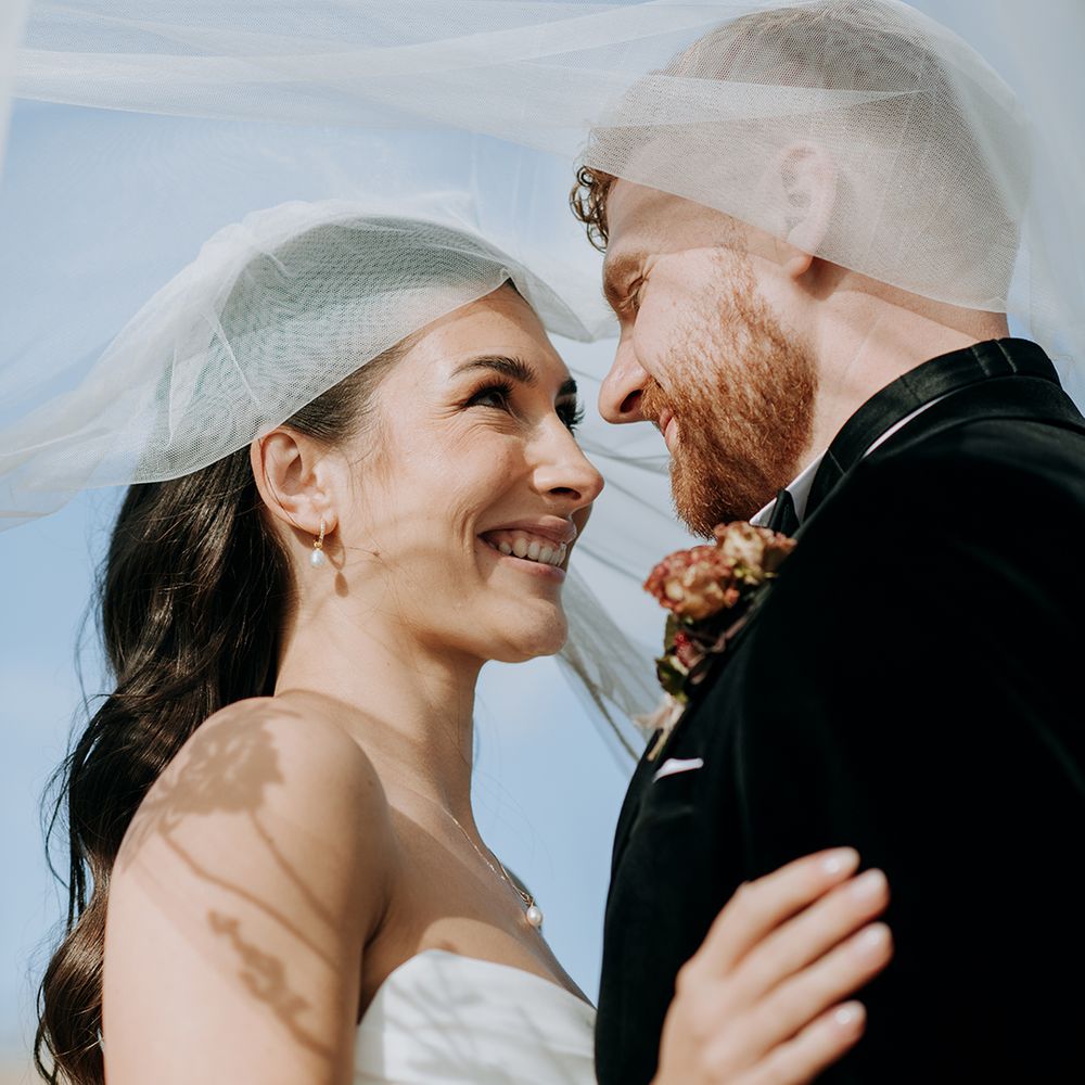 couple-smiles-at-each-other-under-wedding-veil