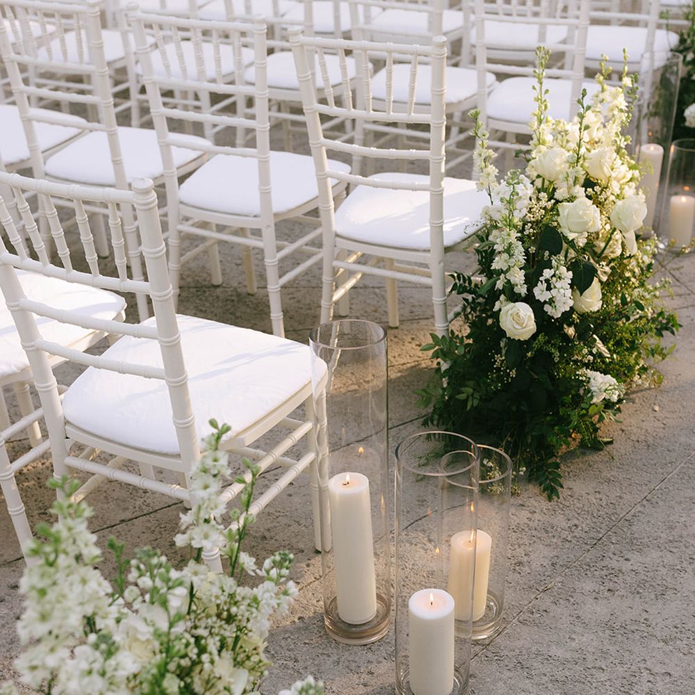 White aisle flower arrangements with candles in hurricane vases