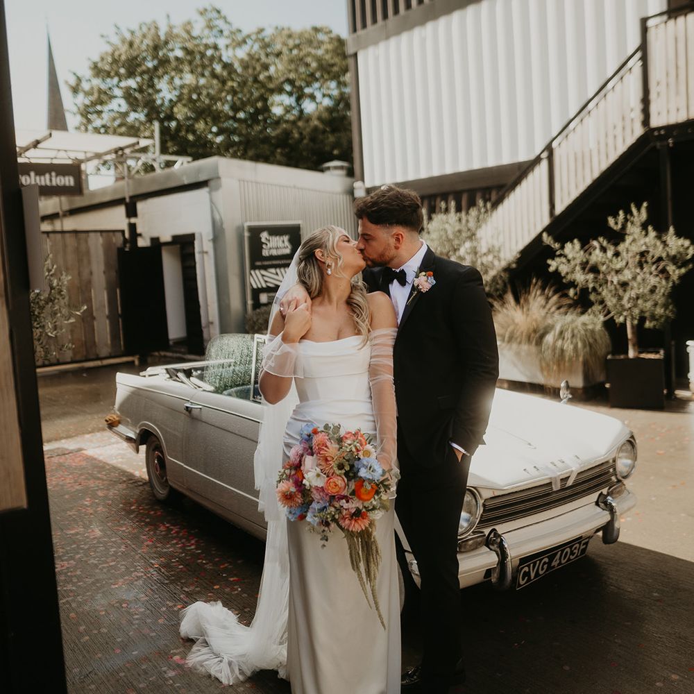 couple-kisses-while-leaning-against-vintage-wedding-car