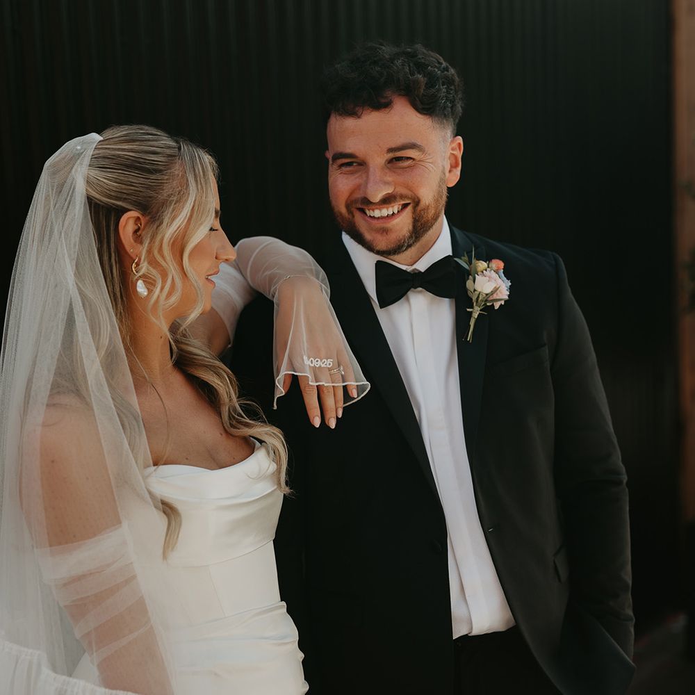 groom-smiles-at-bride-who-wears-embroidered-sleeve-details
