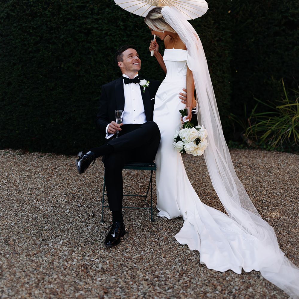 groom-on-seat-with-bride-in-wedding-dress-under-paper-umbrella