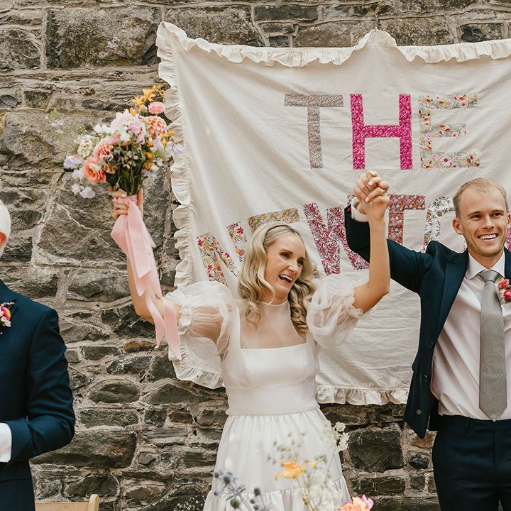bride-and-grooms-raise-their-hands-in-front-of-diy-signage