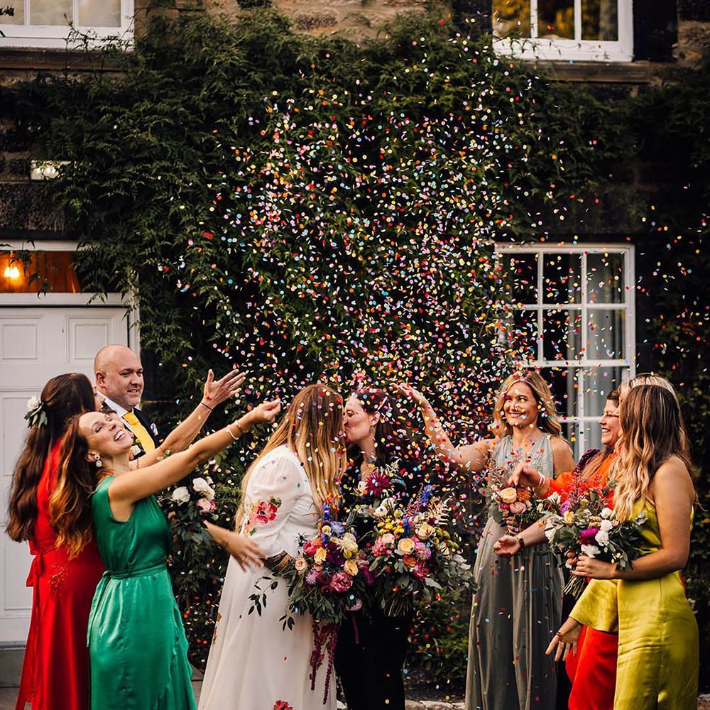 Bridesmaids wearing mismatched wedding dresses throwing colourful confetti