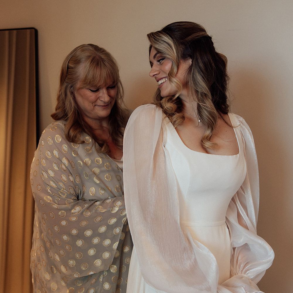 Mother of the bride helps bride into her wedding dress
