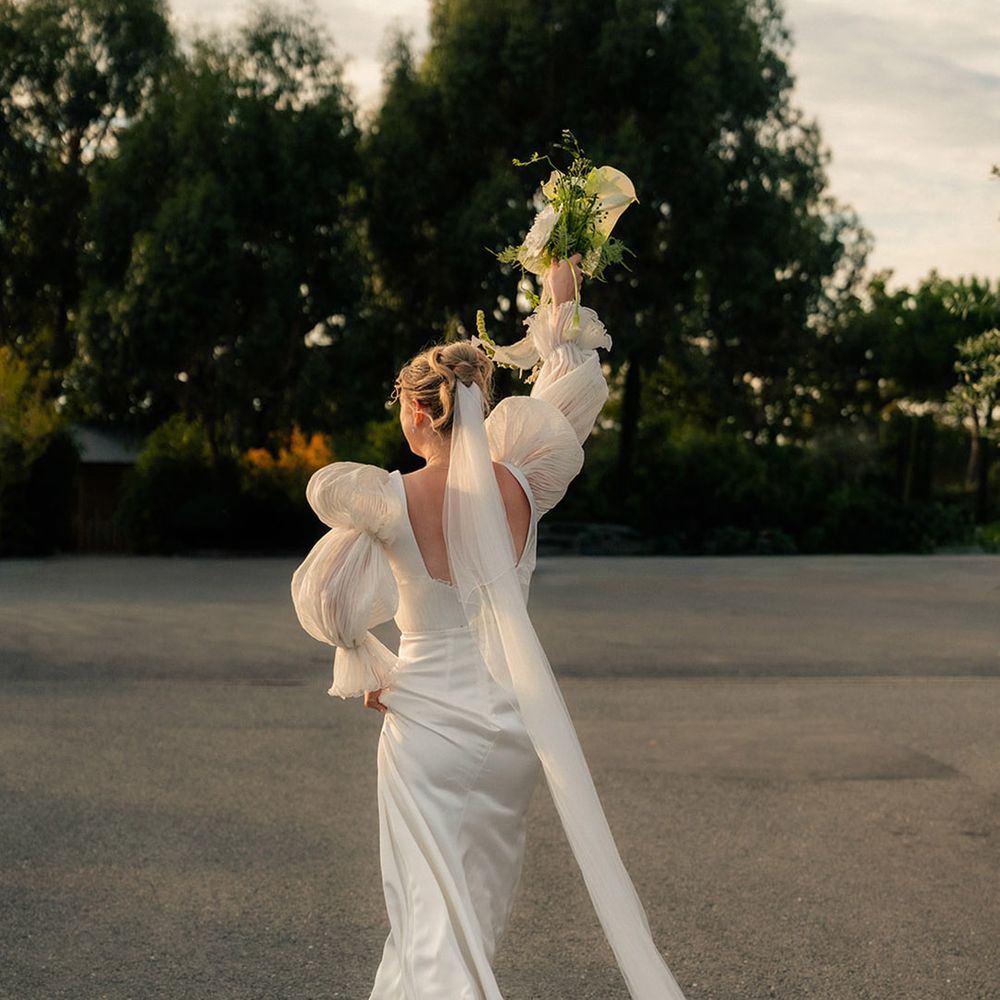 bride-walking-in-sunlight-with-bouquet-in-air.