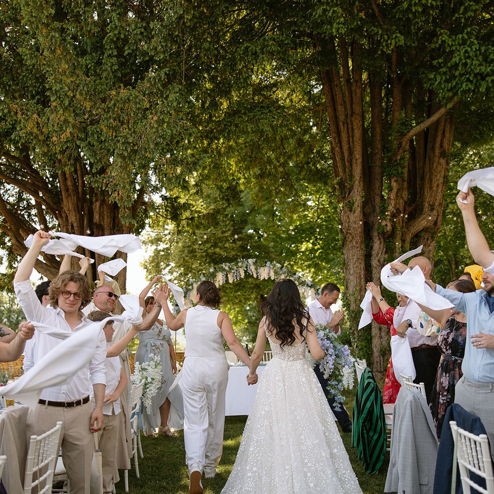 Brides make their entrance to wedding breakfast as guests wave napkins