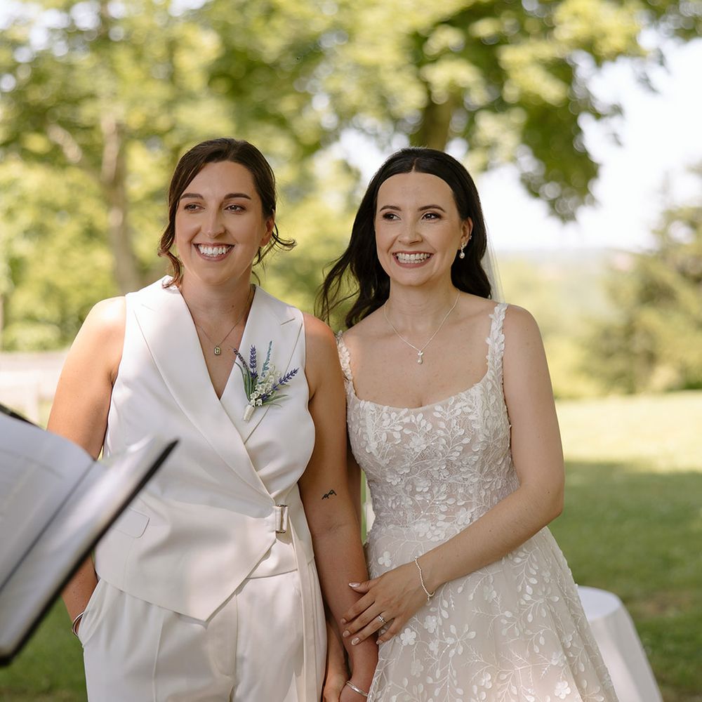 Brides holding hands and smiling for their wedding ceremony