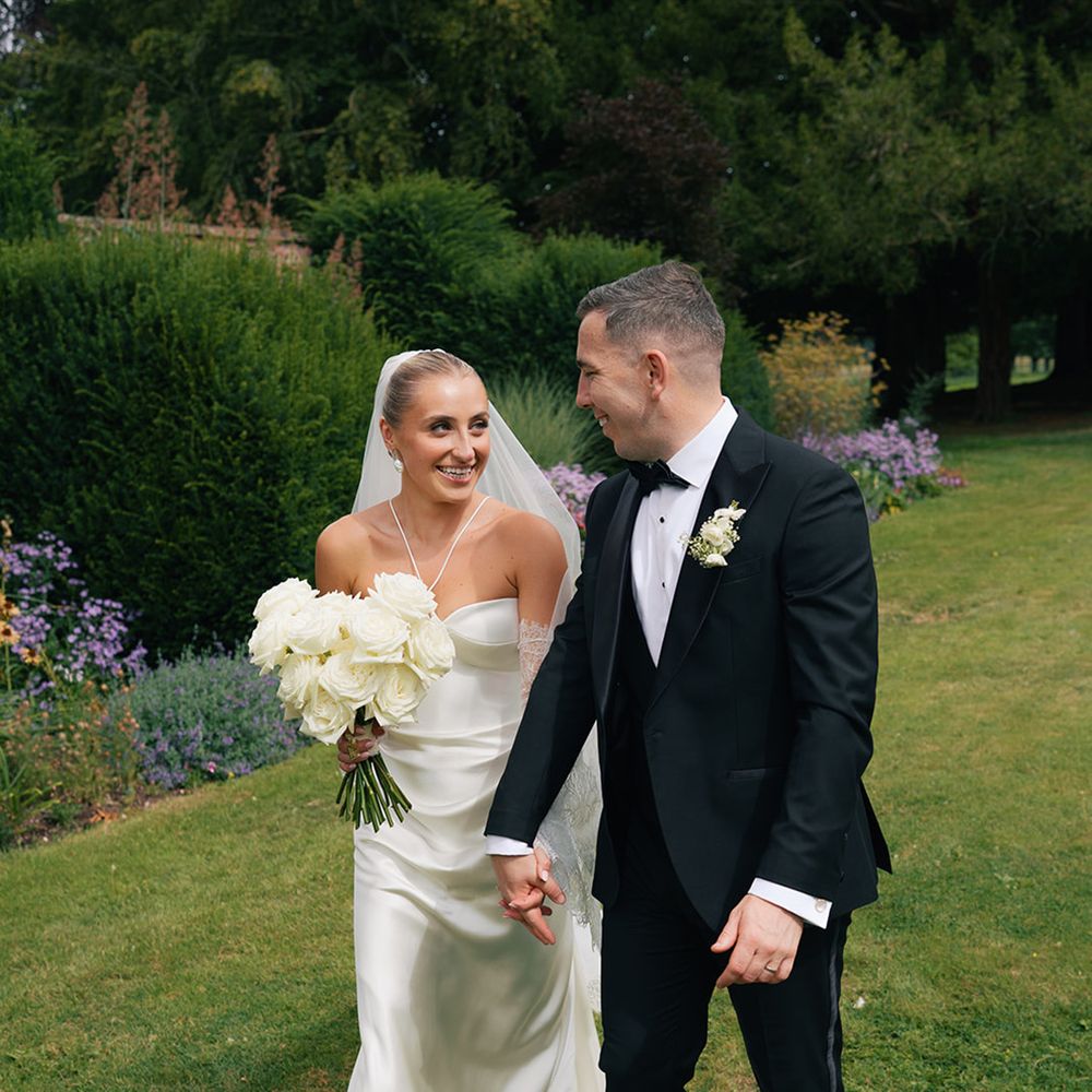 Bride wearing satin halter neck wedding dress with groom in black tuxedo