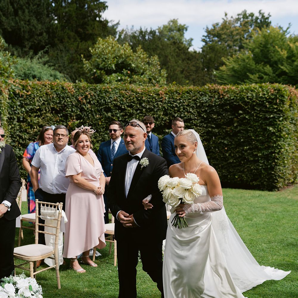 Father of the bride walks bride down the aisle at outdoor wedding
