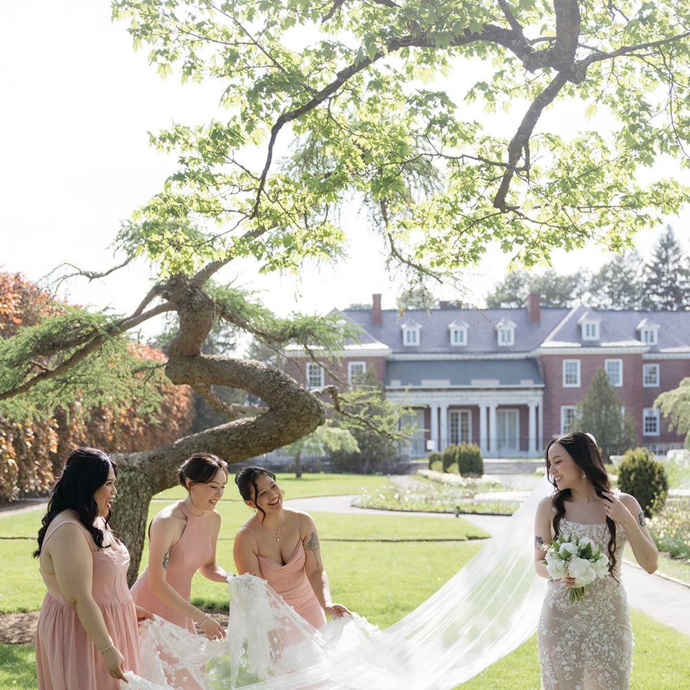 Bridesmaids in pink dresses helping bride with veil 