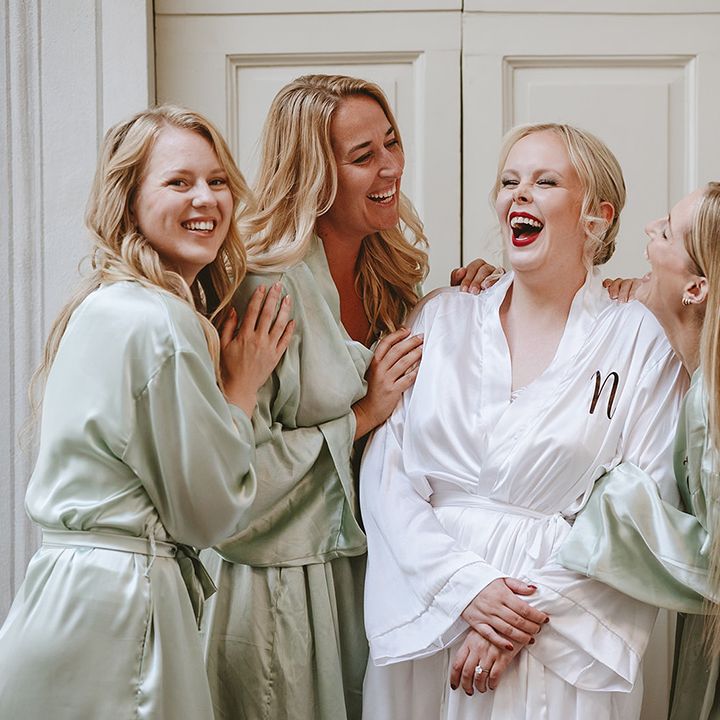 Bridal party laughing together in green satin robes with bride in white robe