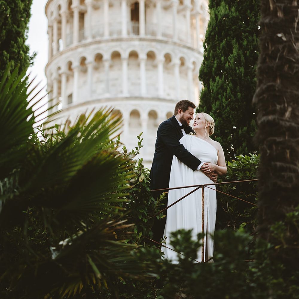 Groom embraces bride in front of the leaning tower of Pisa 
