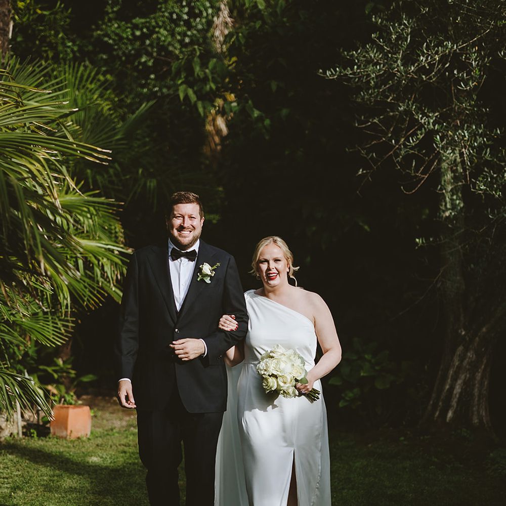Groom in black tuxedo with bride in satin one shoulder wedding dress