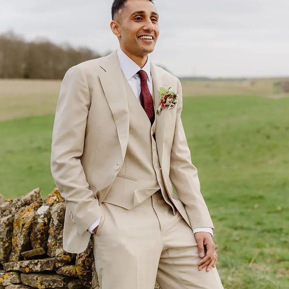 Groom wearing cream three piece suit with burgundy wedding tie