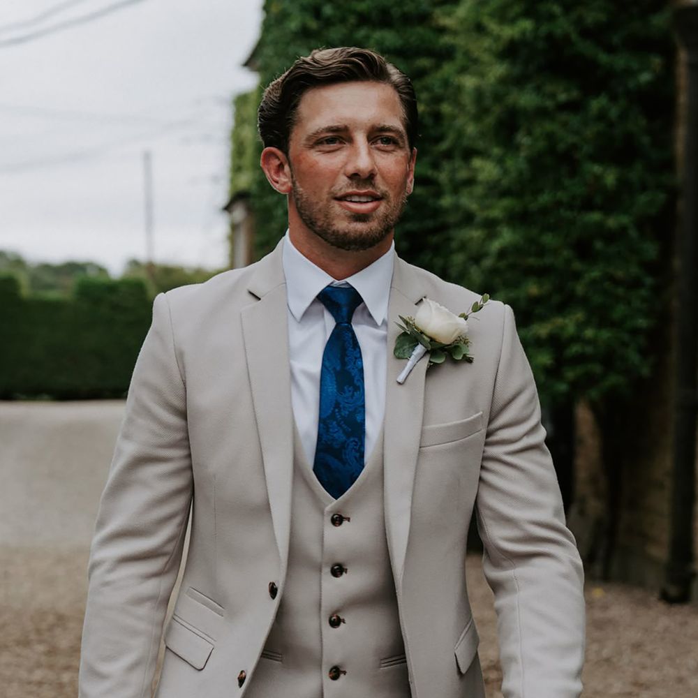 Groom wearing dark blue patterned wedding tie and grey three piece suit