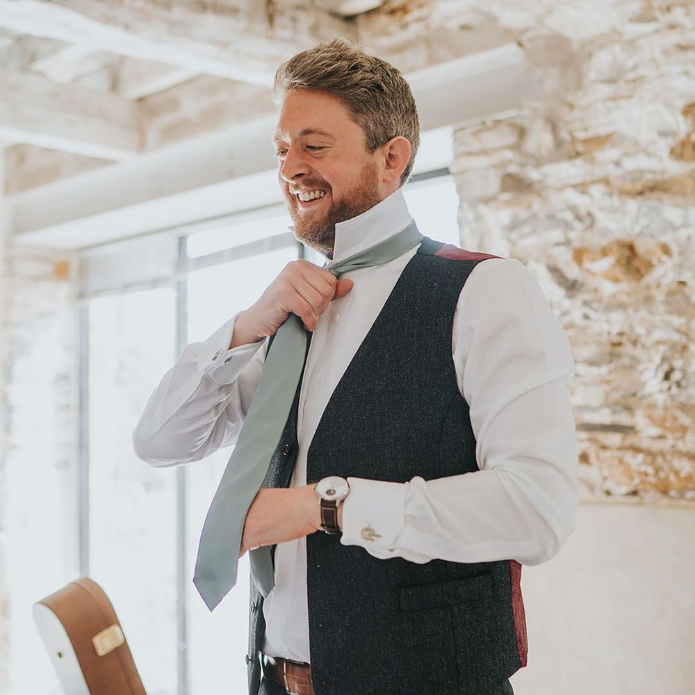 Groom putting on pale green wedding tie