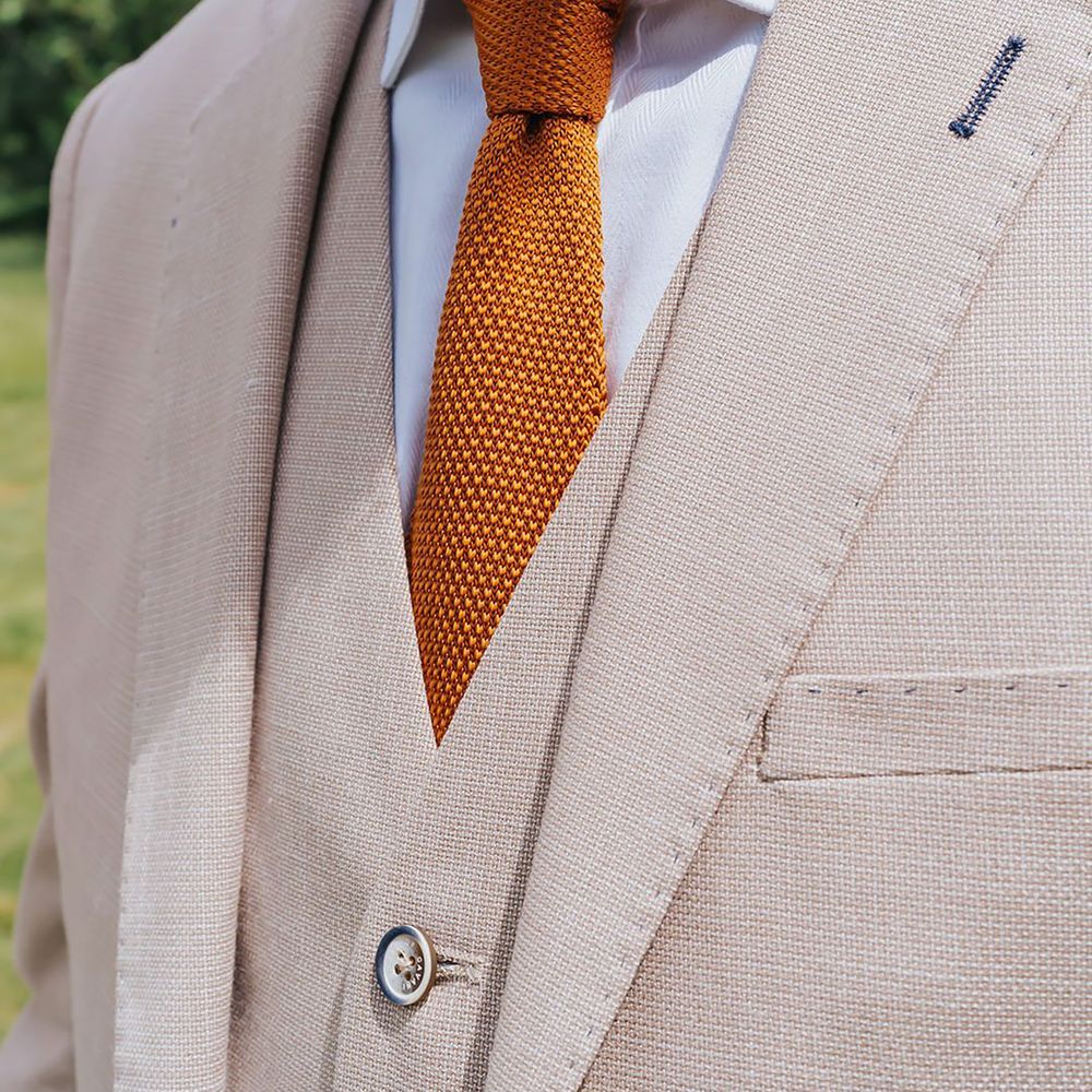 Groom wearing orange waffle wedding tie with beige suit