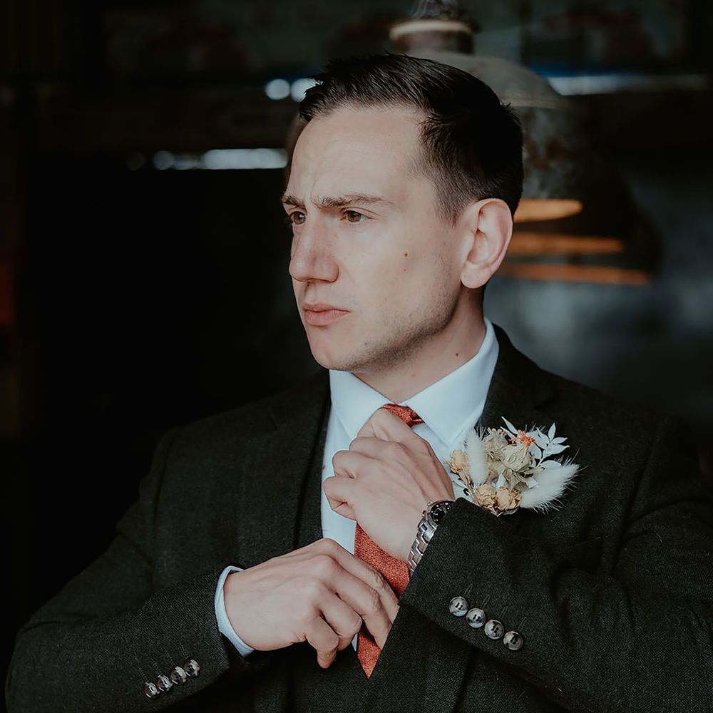 Groom straightening his orange wedding tie
