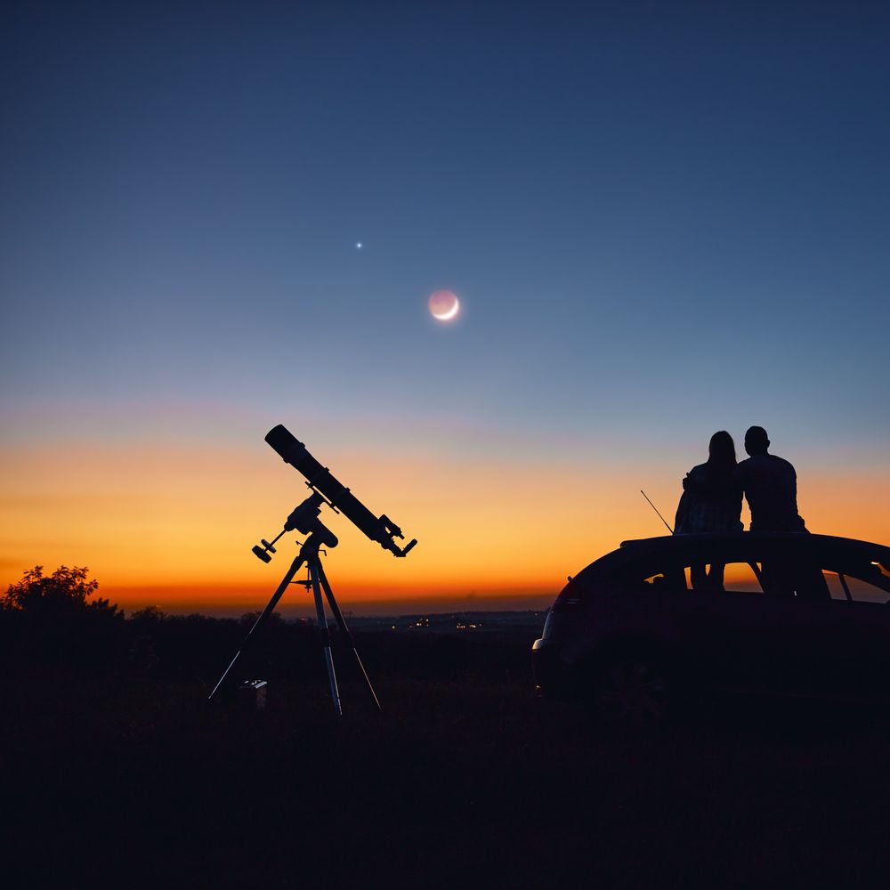 Couple sits with telescope looking into the night sky