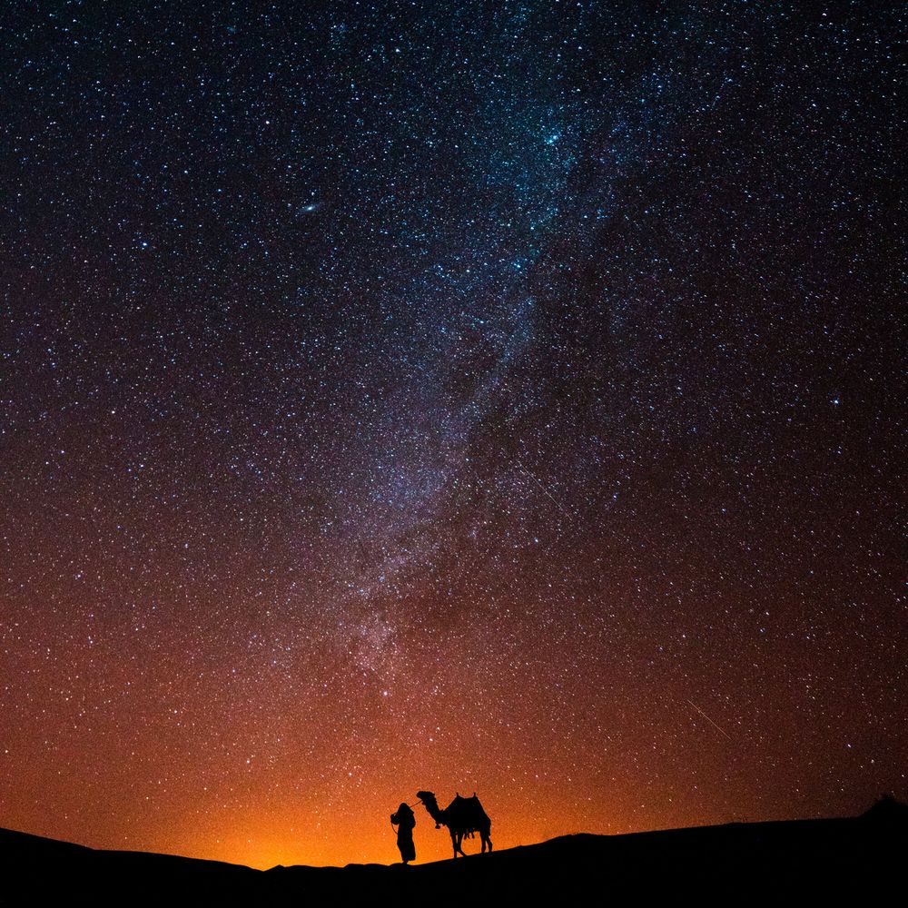 Man walks with camel in the desert under the night sky
