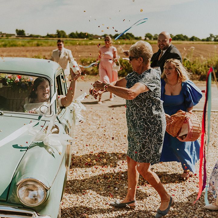 Guests throw confetti over couple in wedding car 