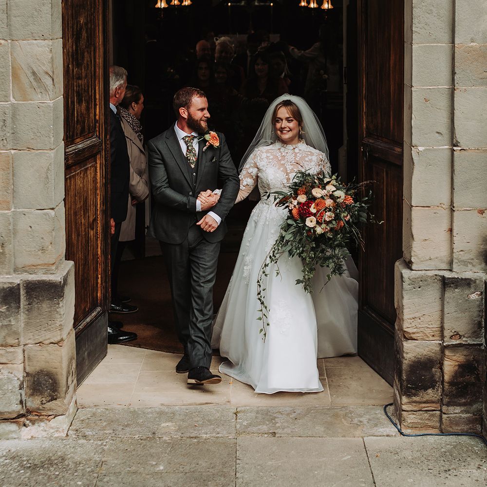 Groom in grey wedding suit with bride in long sleeve lace wedding dress