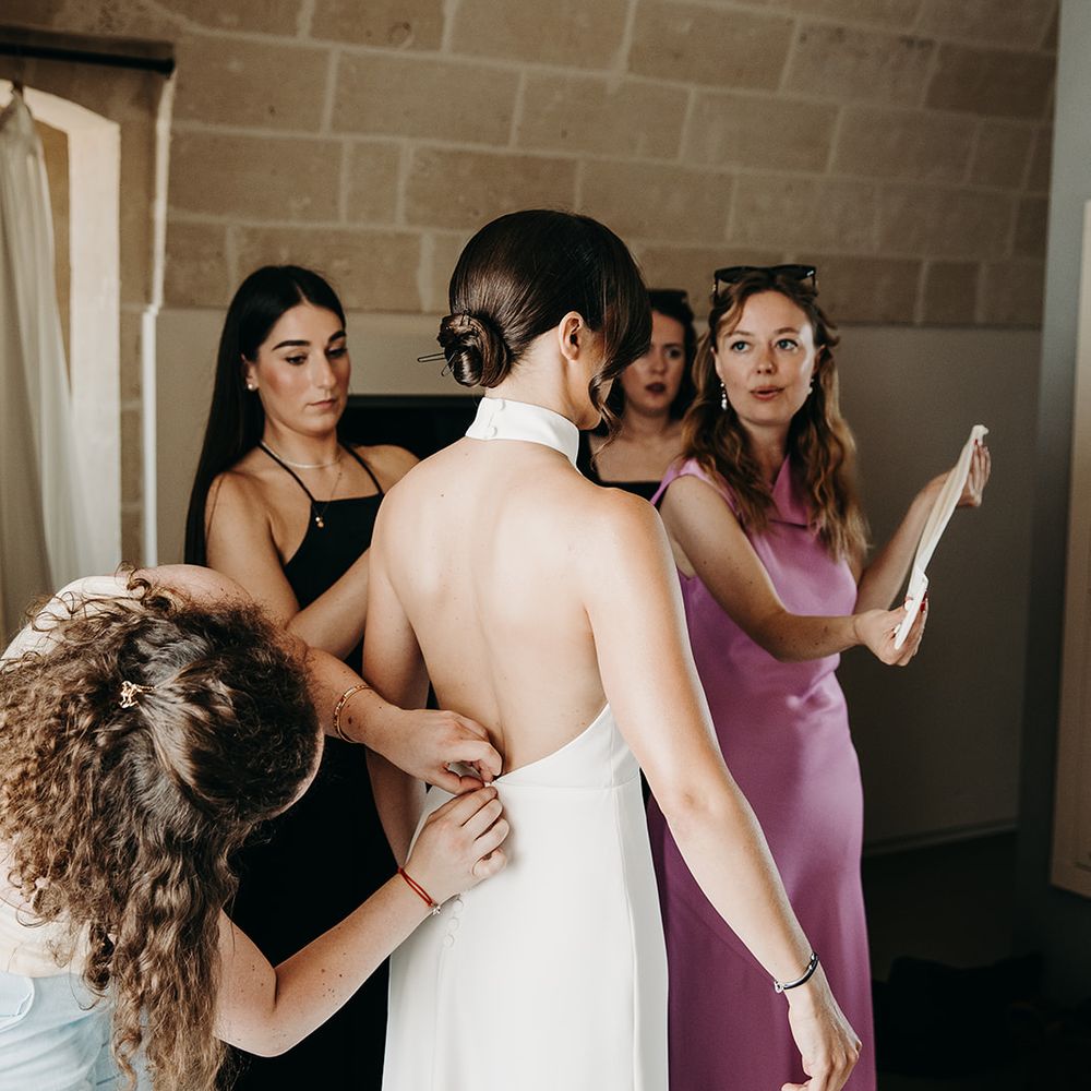 brides dress being done up by bridesmaids