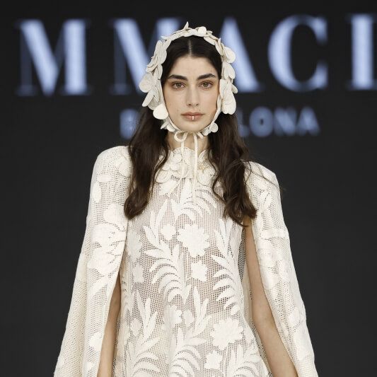 Immaclé lace mini bridal dress with cape sleeves and floral headpiece at Barcelona Bridal Fashion Week 2026