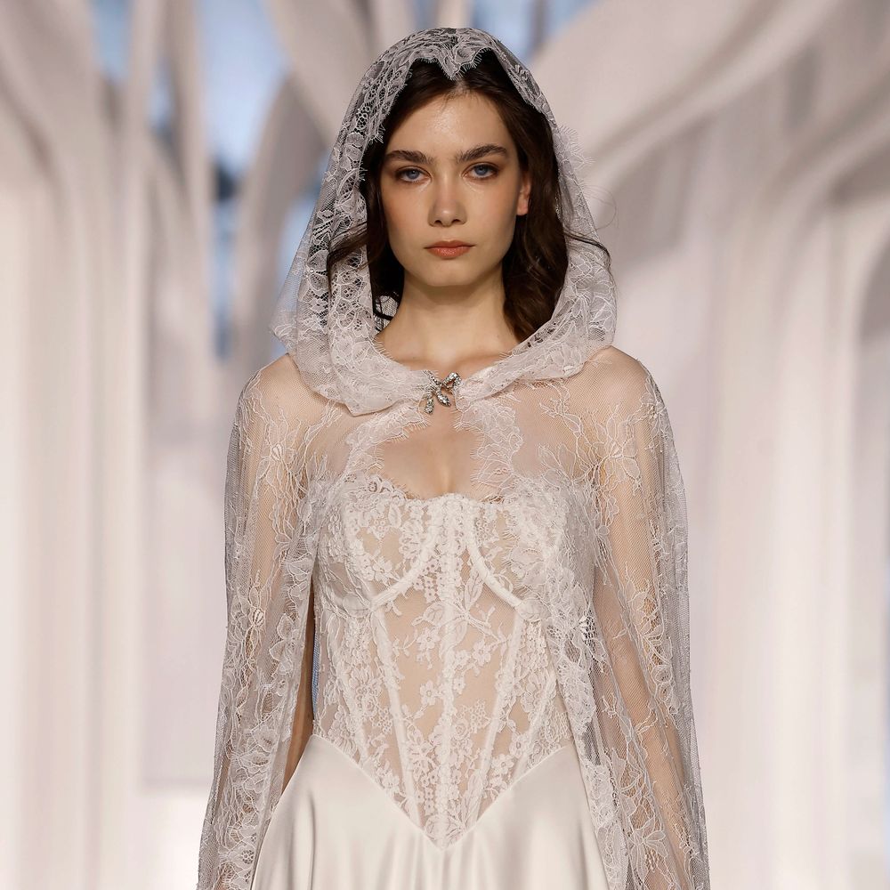 Justin Alexander lace wedding dress with sheer hooded cape and corset bodice at Barcelona Bridal Fashion Week 2026