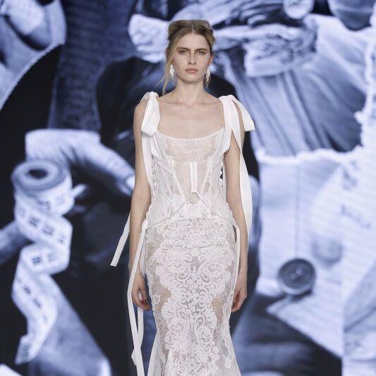 Yolancris sheer lace bridal gown with structured corset, fitted mermaid silhouette and trailing ribbon details at Barcelona Bridal Fashion Week 2026