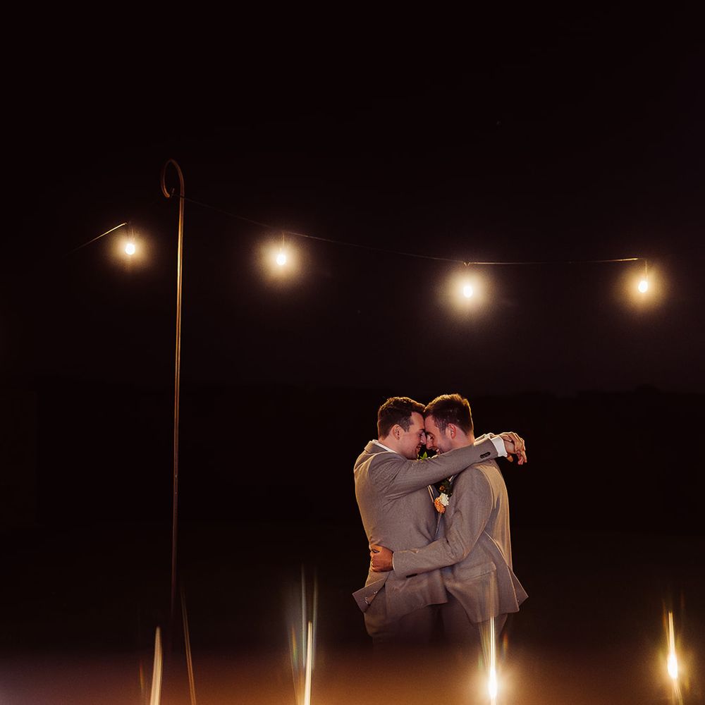 grooms embracing under evening fairylights