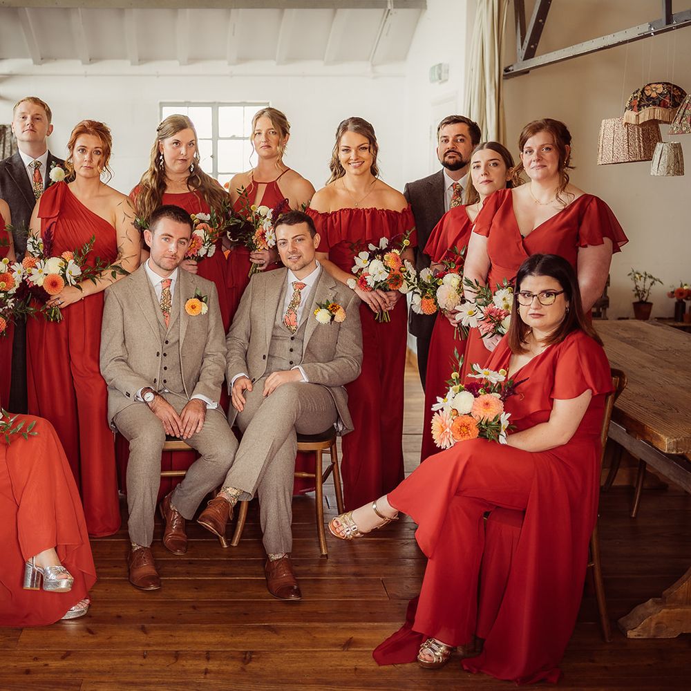 grooms sat down matching suits surrounded red bridesmaids