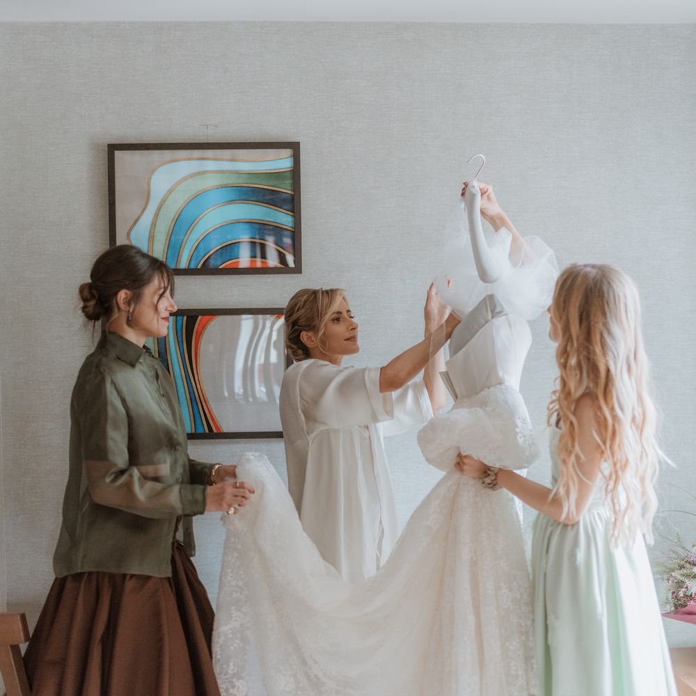 bride getting ready and admiring dress with friends holding lace train