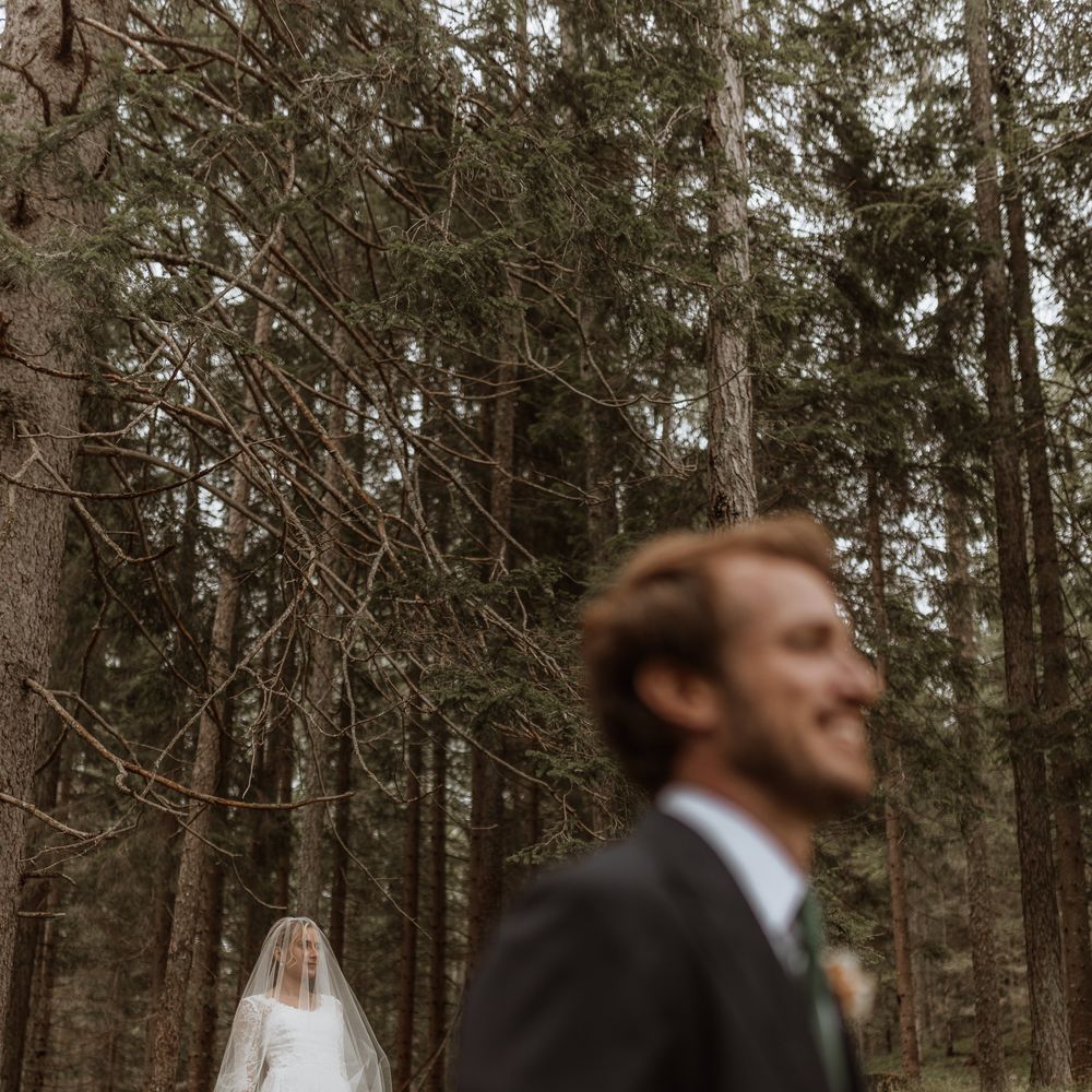 bride in lace veil with smiling groom walking past in forest