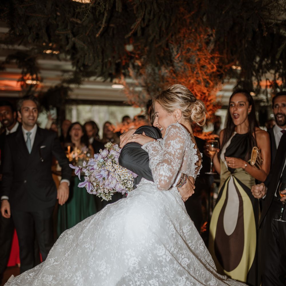 brided in long sleeve lace gown being picked up by groom on dancefloor
