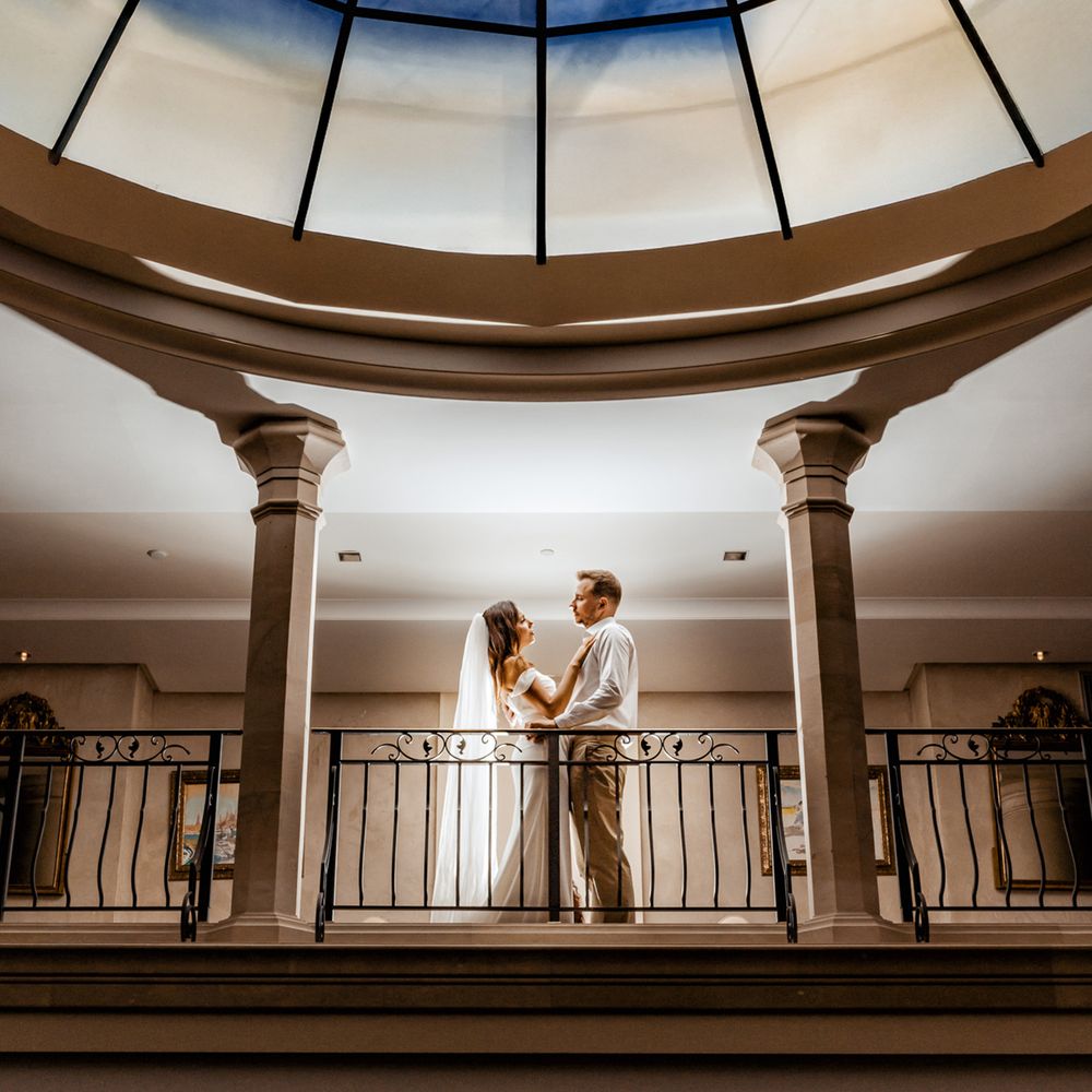 bride and groom embrace under stain glass ceiling