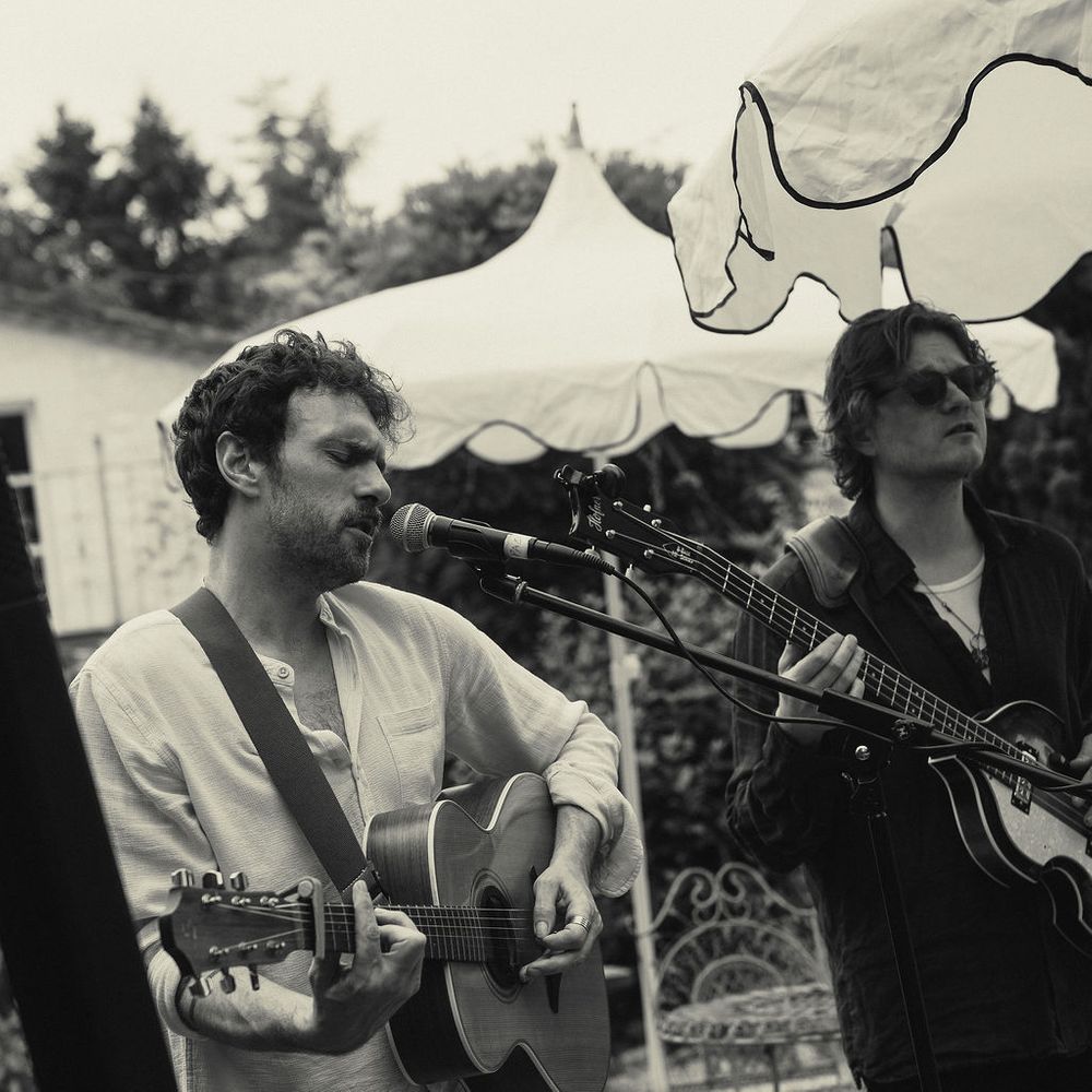 Two acoustic musicians performing outdoors beside a garden marquee in black and white