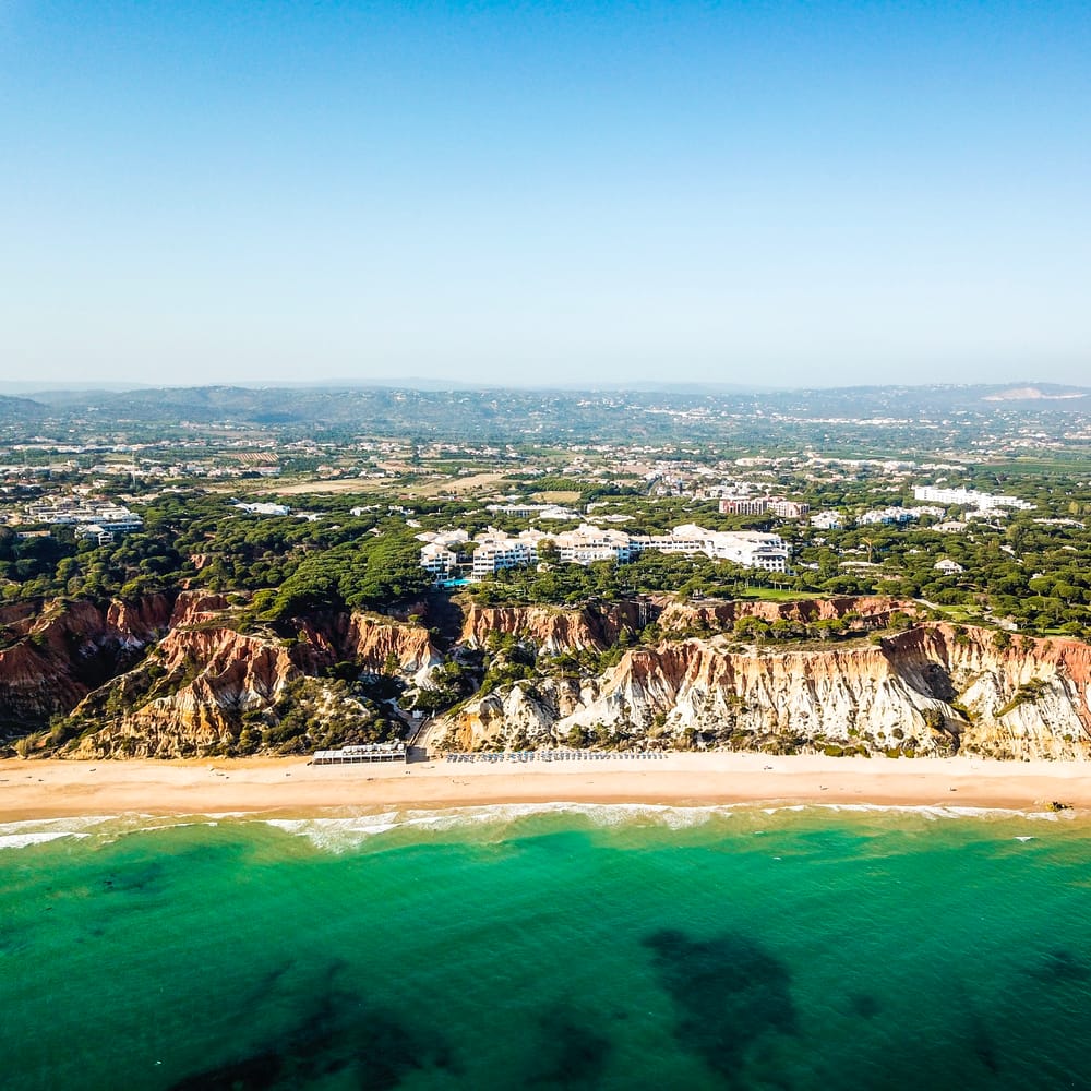 Aerial view of a coastal resort set above golden cliffs and a turquoise sea with sandy beach below