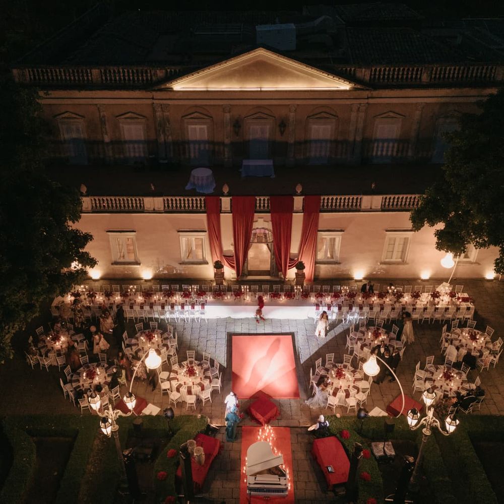Aerial view of an evening reception in a candlelit courtyard with red drapery and a grand piano