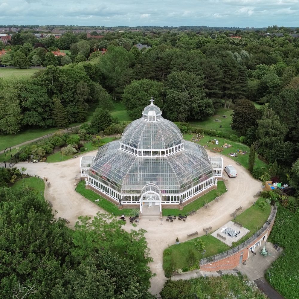 Aerial view of a domed Victorian glasshouse surrounded by manicured lawns and mature trees