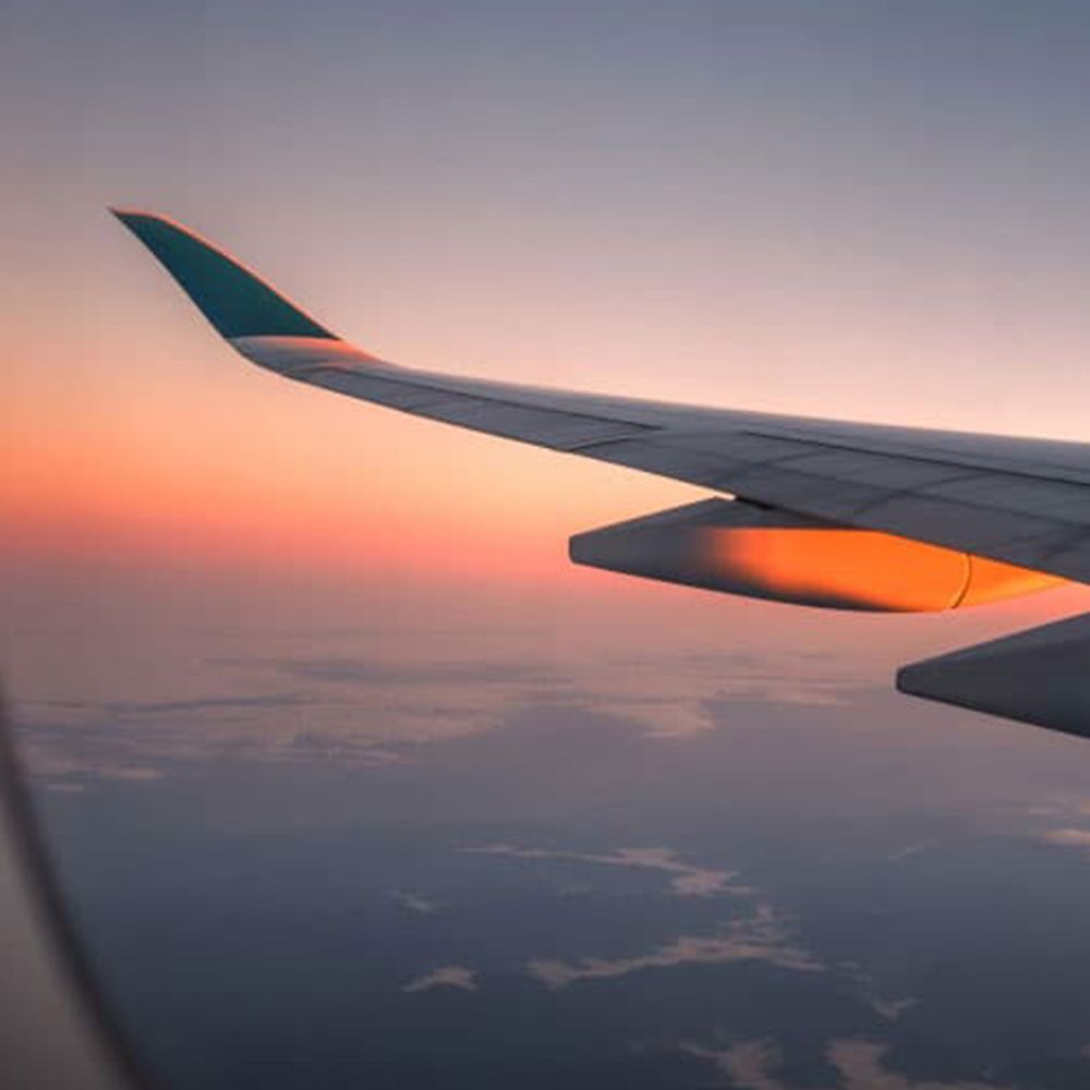 View of an aeroplane wing against a golden sunset sky seen through a cabin window