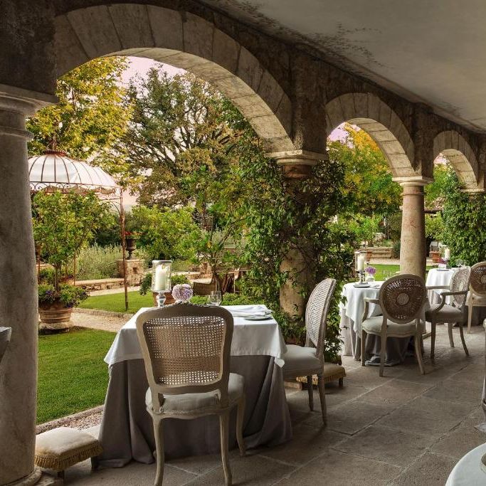 Elegant arched terrace dining area with white-clothed tables, cane chairs and candle lanterns overlooking gardens