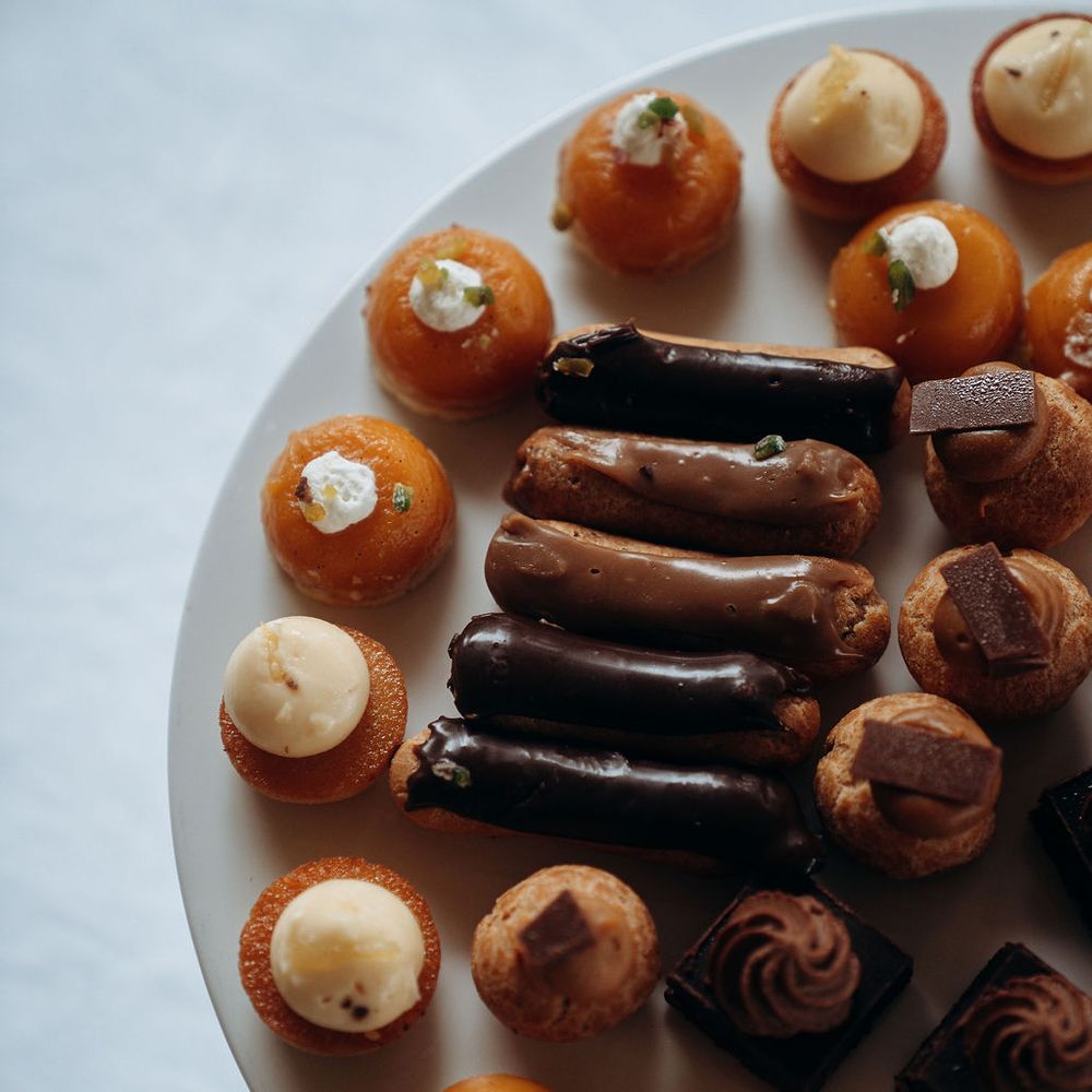 Assortment of miniature chocolate éclairs, choux buns and tarts on a white plate