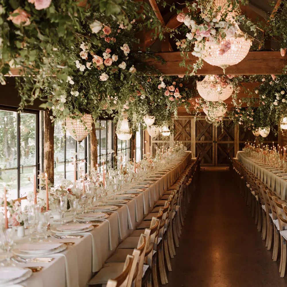 Long barn banquet tables set beneath suspended floral installations and crystal chandeliers