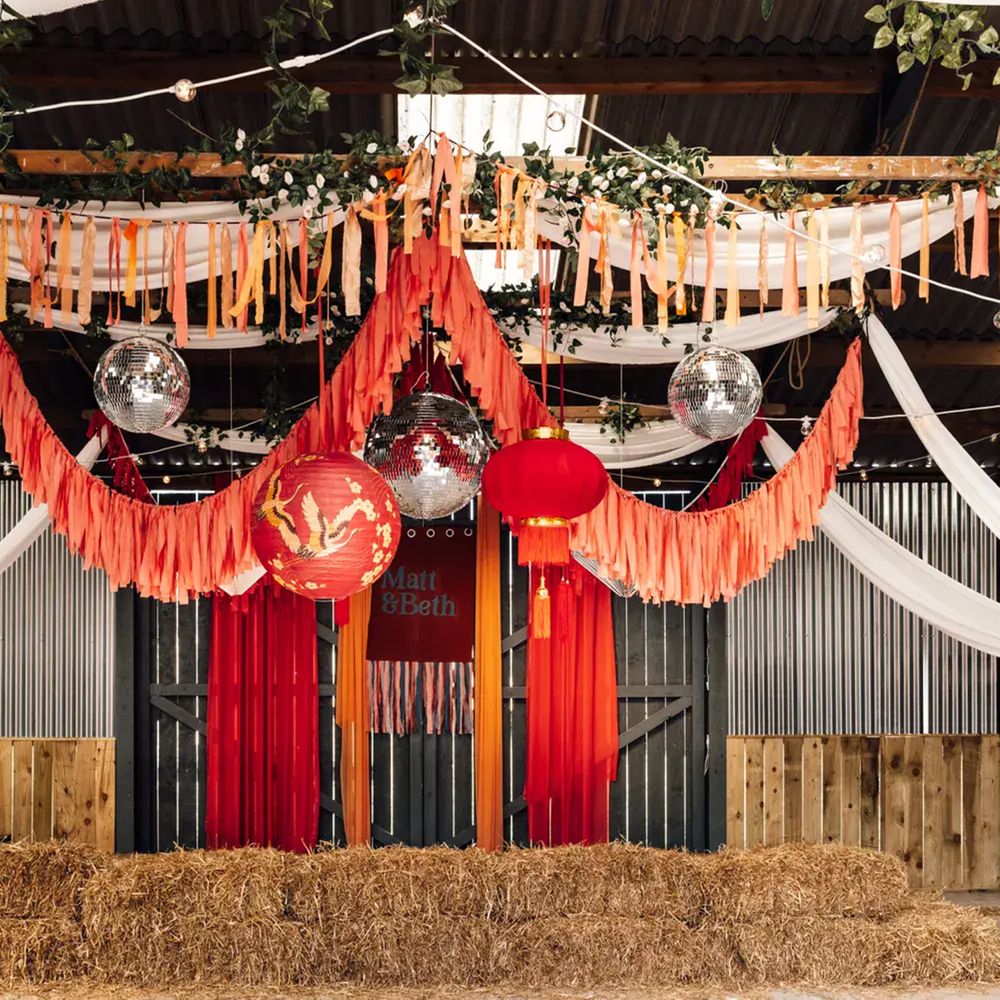 Barn backdrop with red streamers, disco balls, paper lanterns and hay bales beneath draped fabric