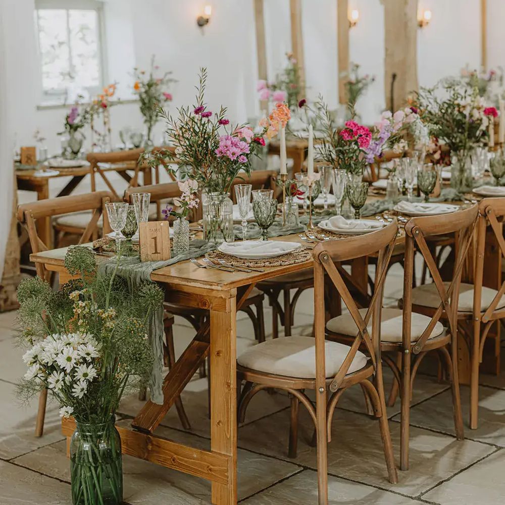 Rustic barn reception with wooden tables, cross-back chairs and colourful wildflower arrangements
