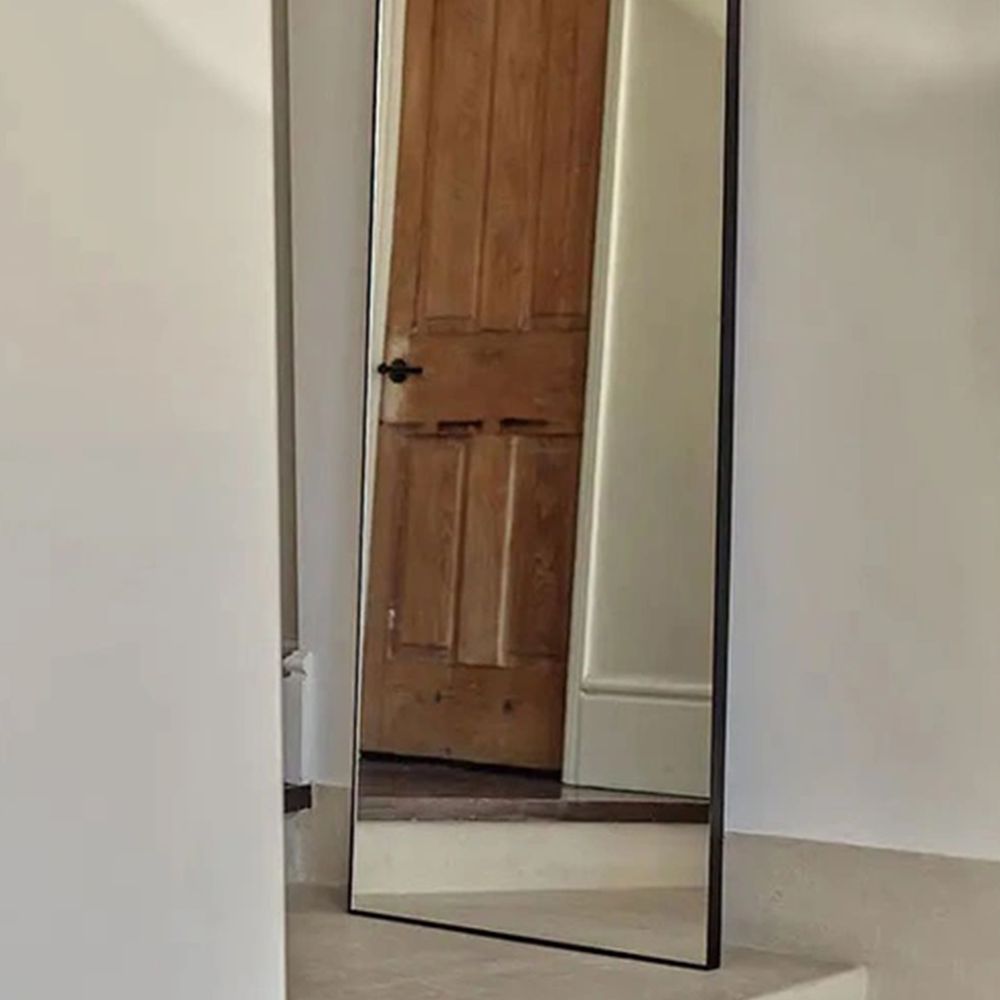 Black-framed arched full-length mirror reflecting a wooden panelled door in a neutral room