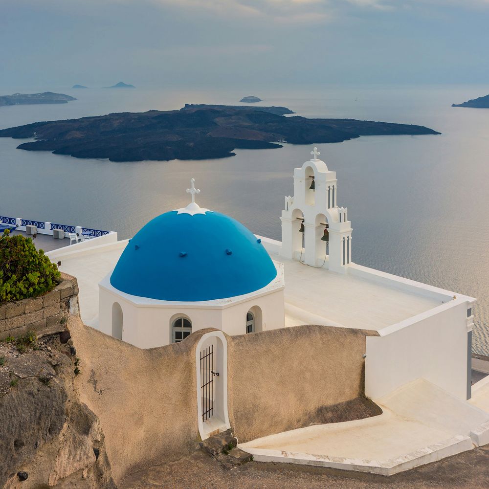 Blue-domed whitewashed church with a bell tower overlooking the sea and distant islands
