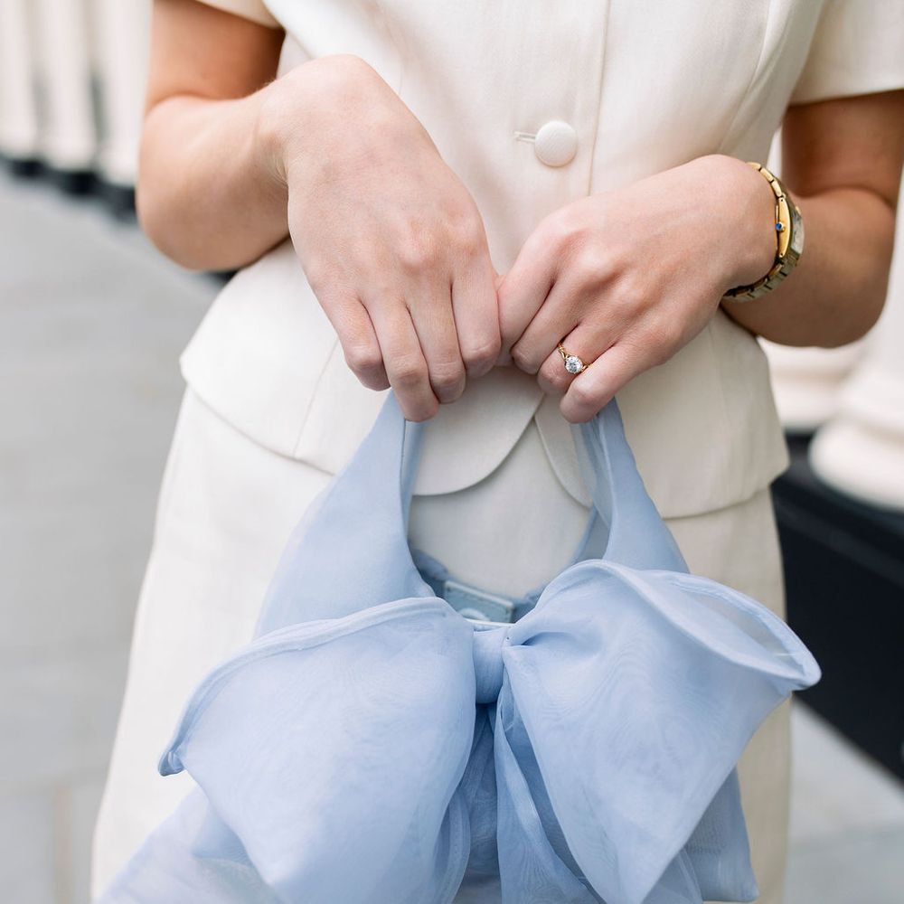 Woman in cream tailored dress holding a pale blue organza bow handbag