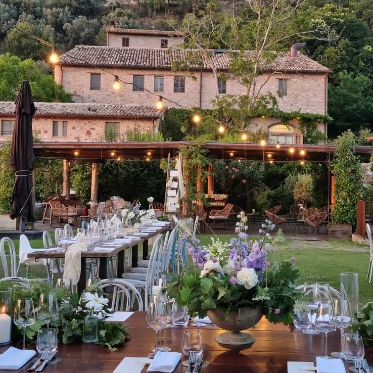 Outdoor wedding tables with lilac and white florals set before a rustic stone farmhouse at dusk